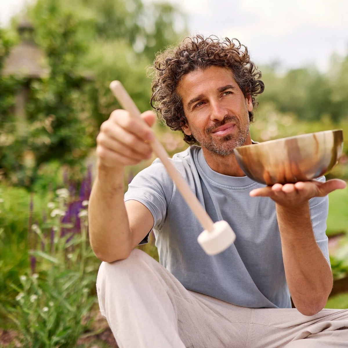 Mann im Garten hält Klangschale und Hess Sound Filzschlägel